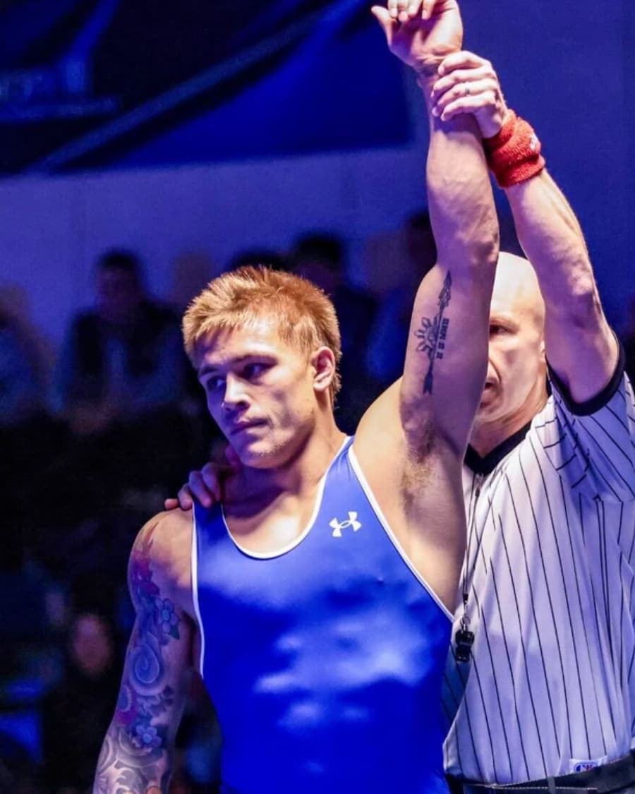A referee raises a wrestler's arm after a win, under arena lights.